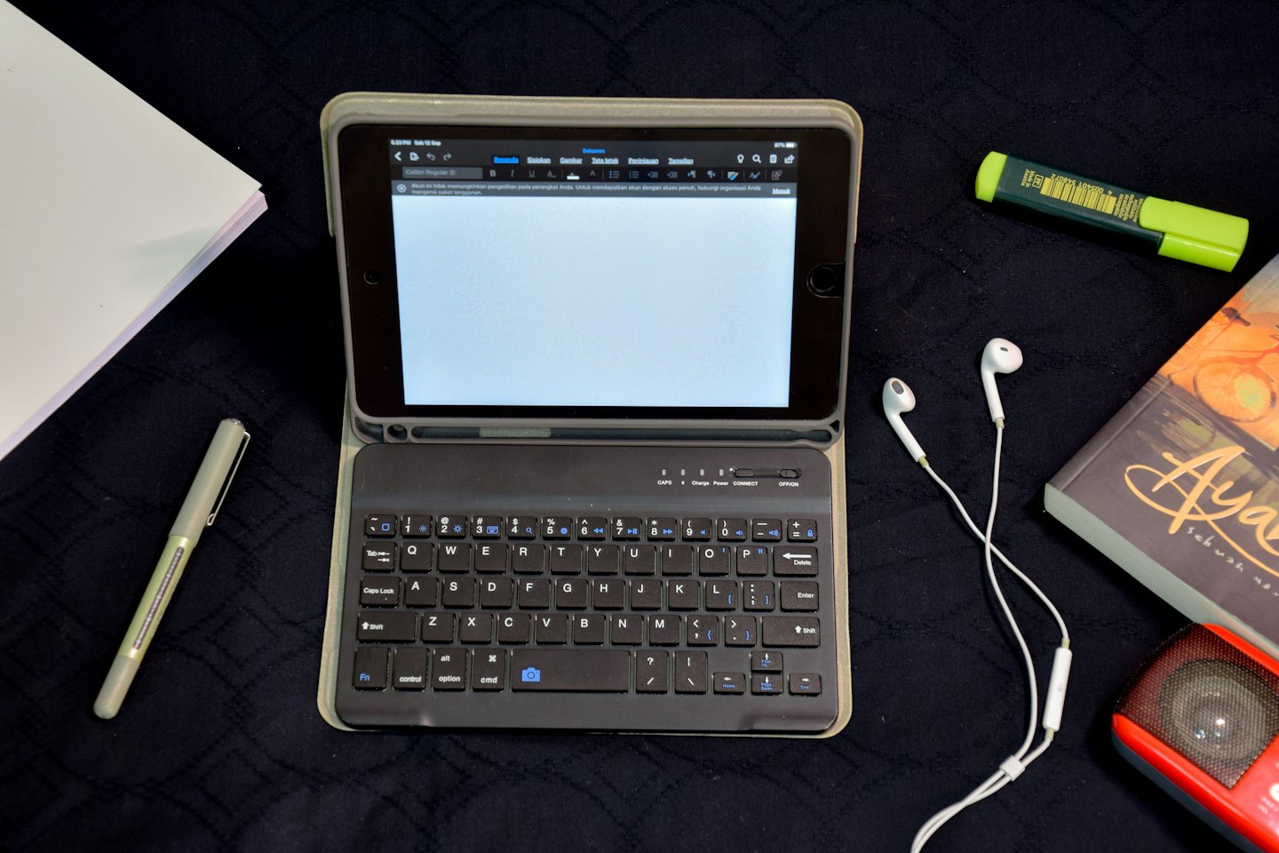 Tablet, pena, dan perlengkapan kantor tersusun di atas permukaan gelap.